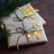 Homemade Christmas gifts in kraft paper with handmade tags and a Christmas tree on dark brown wooden surface.