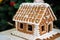 Homemade Christmas Gingerbread House in the snow. Decorated Christmas tree in the background