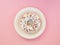 Homemade circle donut with white icing and choclate rainbow sprinkles on a trendy pink background and white plate