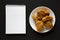 Homemade crispy oven baked fried chicken on a white plate, blank notepad over black background, top view. Copy space