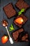 Homemade dark chocolate brownies decorated with strawberries and mint leaves over black slate background, top view.