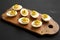 Homemade Deviled Eggs with Chives on a rustic wooden board on a black background, side view
