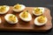 Homemade Deviled Eggs with Chives on a rustic wooden board on a black surface, side view. Close-up