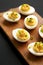 Homemade Deviled Eggs with Chives on a rustic wooden board on a black surface, side view. Close-up