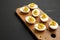 Homemade Deviled Eggs with Chives on a rustic wooden board on a black surface, side view. Copy space