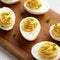 Homemade Deviled Eggs with Chives on a rustic wooden board on a white wooden surface, side view. Close-up