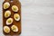 Homemade Deviled Eggs with Chives on a rustic wooden board on a white wooden surface, top view. Flat lay, overhead, from above.