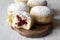 Homemade donuts with jelly and powdered sugar on wooden board on white wooden background, side view