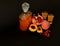 Homemade fruit liqueur in a bottle and two glasses on a black background, next to pieces of a ripe peach and a broken pomegranate