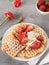 Homemade golden brown waffle topped with strawberries, nuts and whipped cream
