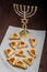 Homemade gomentashi cookies for the Jewish holiday of Purim on a checkered napkin next to the menorah.