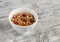 Homemade granola in white bowl on bright wooden surface.