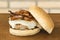 Homemade hamburger with cheese and bacon and the bun on the side over wooden cutting board and brick background