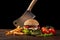 Homemade hamburger close-up with beef, tomato, lettuce, cheese, onion and french fries on wooden table. In the burger stuck a