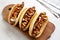 Homemade hot dogs with chicken sausage, ketchup and mustard on a rustic wooden board on a white wooden surface, low angle view.