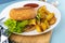 Homemade imperfect burger with potatoes and salad on a plate. Food on the table in a white plate on a wooden board.