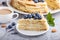 Homemade layered Napoleon cake with milk cream. Decorated with blueberry, almonds, walnuts, hazelnuts, mint on a gray concrete