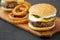 Homemade Mississippi Slug Burger with onion rings on a rustic wooden board on a black surface, side view. Close-up