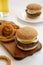 Homemade Mississippi Slug Burgers with onion rings and glass of cold beer on a white wooden surface, side view. Close-up