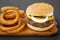 Homemade Mississippi Slug Burgers with onion rings on a rustic wooden board on a black surface, side view. Close-up