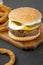 Homemade Mississippi Slug Burgers with onion rings on a rustic wooden board on a black surface, side view. Close-up