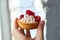 Homemade muffin in a brown sugar basket with white cream and fresh red raspberry in hand on blurred gray background close up