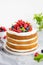 Homemade naked layered vanilla cake with whipped cream and fresh berries on top on a gray concrete background. Summer cake.