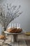 Homemade nuts bundt cake with powder sugar, candles and bouquet of fresh willows on wooden table. Rustic style