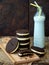 Homemade Oreo chocolate cookies with white marshmallow cream and botle of milk on dark background.