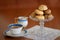 Homemade panellets in vintage glass stand, lace doily, porcelain coffee cup and milk jar. Image with copy space.