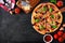 Homemade pizza with pepperoni, vegetables and basil, top view, corner border against a dark background with copy space