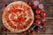 Homemade pizza with salami and red chilli pepperoni is lying on a wooden surface of pine planks next to tomatoes, pieces of