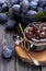Homemade plum jam in a glass jar and fresh blue plums in a bowl on a dark rustic wooden background with copy space top view.