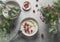 Homemade porridge bowl with milk raspberries at grey concrete kitchen table with bowls, cutlery and beautiful summer flowers.