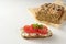Homemade protein bread with seeds on baking paper and sandwich with curd, tomatoes and parsley garnish on a white table, healthy