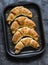 Homemade puff pastry walnuts brown sugar croissants on a baking sheet on a dark background, top view