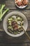 Homemade rice dish with leek and meat in bowl with golden fork at rustic wooden kitchen table with vegetable and fried bacon.