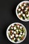 Homemade Shepherds salad with cucumbers, feta and parsley in white bowls on a black surface, top view. From above, overhead, flat