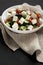 Homemade Shepherds salad with cucumbers, parsley and feta in a white bowl on a black surface, side view. Closeup