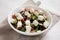 Homemade Shepherds salad with cucumbers, parsley and feta in a white bowl on a white wooden surface, side view. Close-up