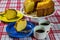 Homemade simple cake with yellow and blue dishes on the side and cups of coffee on the table with white and red checkered tableclo