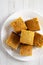 Homemade Sliced Cornbread Ready to Eat on a white plate on a white wooden background, top view. Flat lay, overhead, from above.