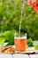 Homemade strawberry compote pouring in glass from decanter with pretzels on white wooden table in garden