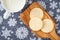 Homemade sugar cookies on a wood paddle shaped cutting board, snowflake background, mug of milk