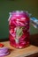 Homemade sweet and spicy pickled red onions sliced in a large glass jar with rosemary