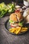 Homemade tasty burger with chicken, lettuce, mozzarella and tomatoes served with french fries potatoes on rustic kitchen table bac