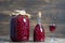 Homemade tincture of red cherry in a glass bottle, jar and a wineglass on wooden background, Ukraine, close up