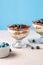 Homemade tiramisu with blueberries in glass jars. Traditional unbaked Italian dessert on blue background. Individual trifle.