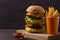 Homemade triple decker burger and fries on dark wooden background.