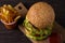 Homemade triple decker burger and fries on dark wooden background.